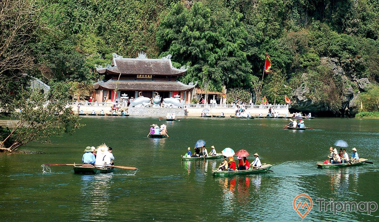 ảnh chụp mọi người đang ngồi trên thuyền dưới sông, ngôi chùa 2 vòm mái màu nâu bên bờ sông Đáy, cây cối xanh phủ đầy cách đồi