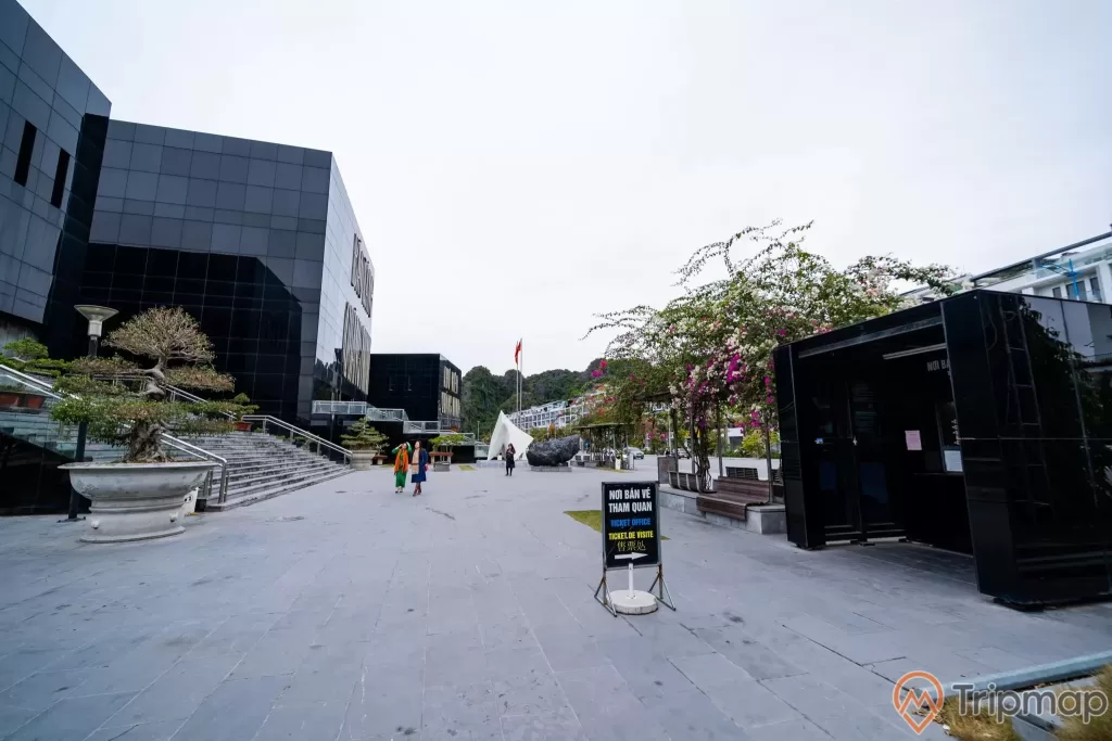Bảo tàng Quảng Ninh, nền đất màu xám, chậu cây, bậc thang màu xám, người đang đi trên nền đất màu xám, cây hoa giấy, quầy bán vé, ảnh chụp ban ngày