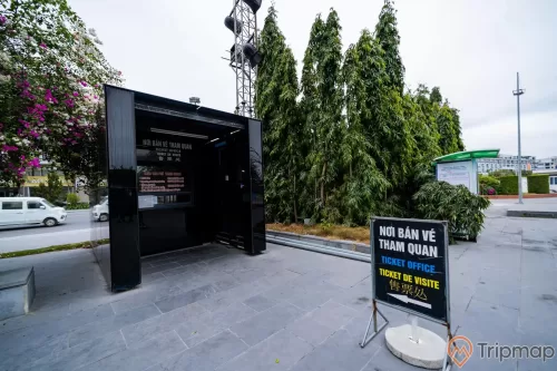 Bảo tàng Quảng Ninh, nền đường màu xám, bảng chỉ dẫn màu đen, nhiều cây xanh, ô tô màu trắng, cây hoa giấy, ảnh chụp ban ngày