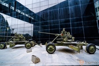 Bảo tàng Quảng Ninh, vũ khí quân sự sơn màu xanh, nền gạch màu xám, tòa nhà màu đen, ảnh chụp ban ngày