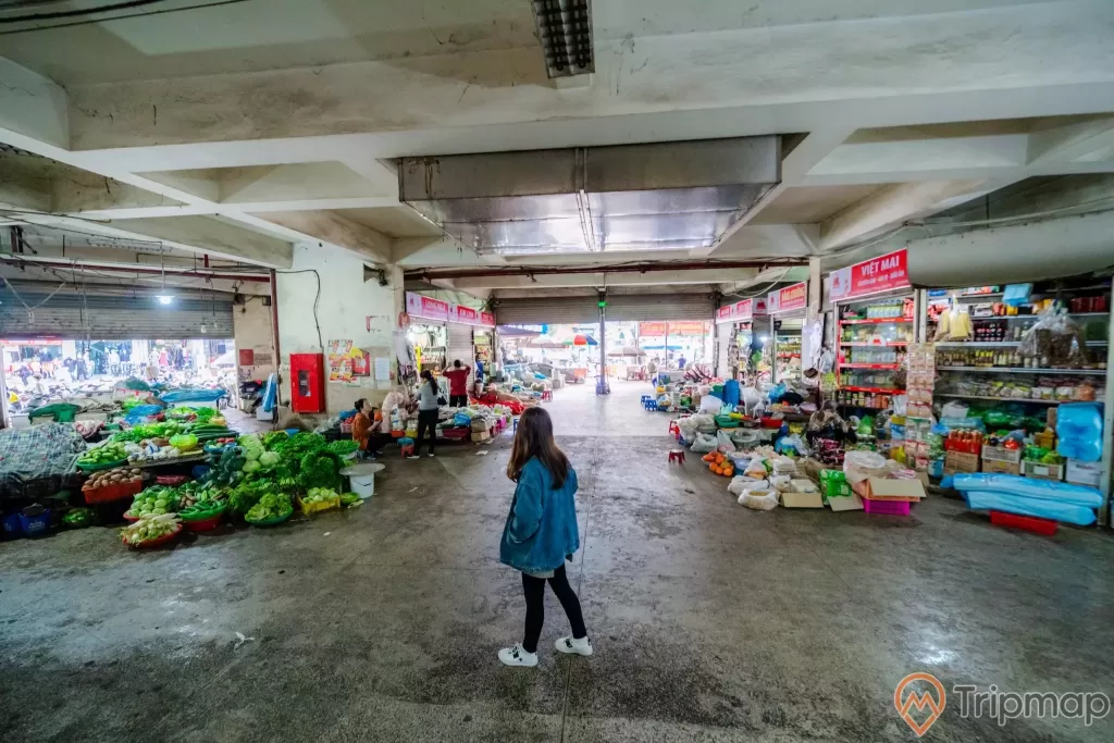 Chợ Hạ Long 2 , Chợ Loong Toòng, cô gái mặc áo xanh đang đứng trên nền đường màu xám, trần nhà màu trắng, ảnh chụp ban ngày