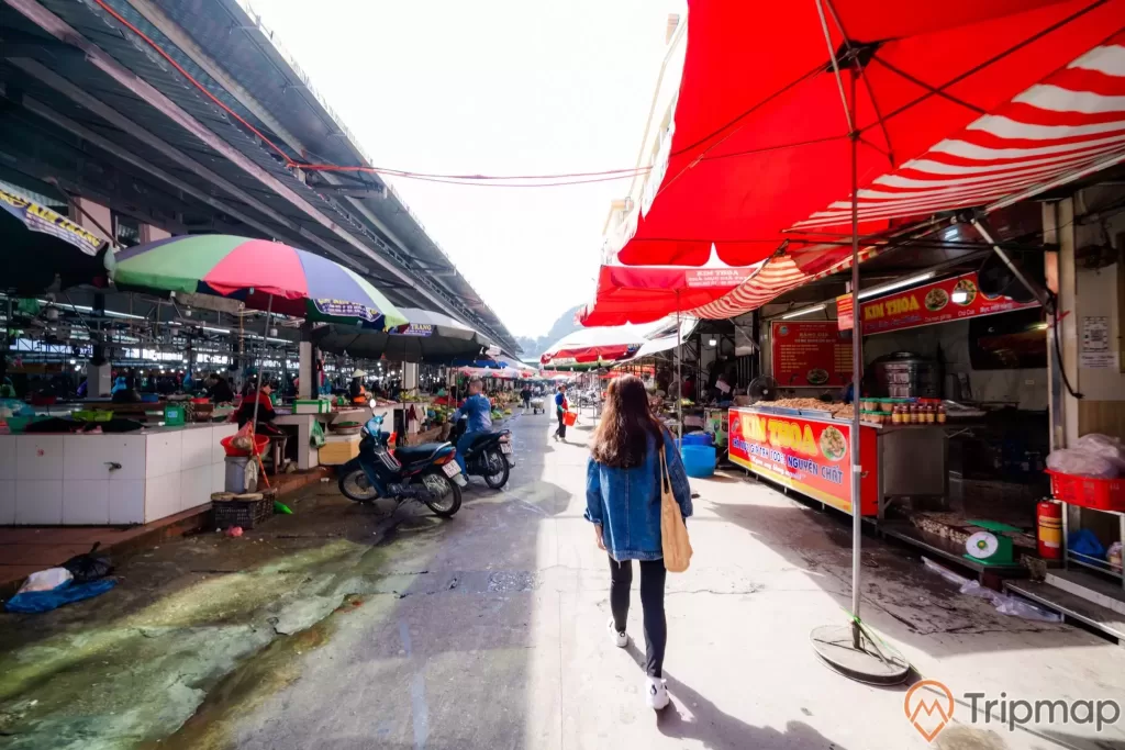 Chợ Hạ Long, Chợ Hòn Gai, cô gái mặc áo xanh đang đi trên nền đường màu xám, nhiều ô màu đỏ, nhiều xe máy, trời nắng, ảnh chụp ban ngày
