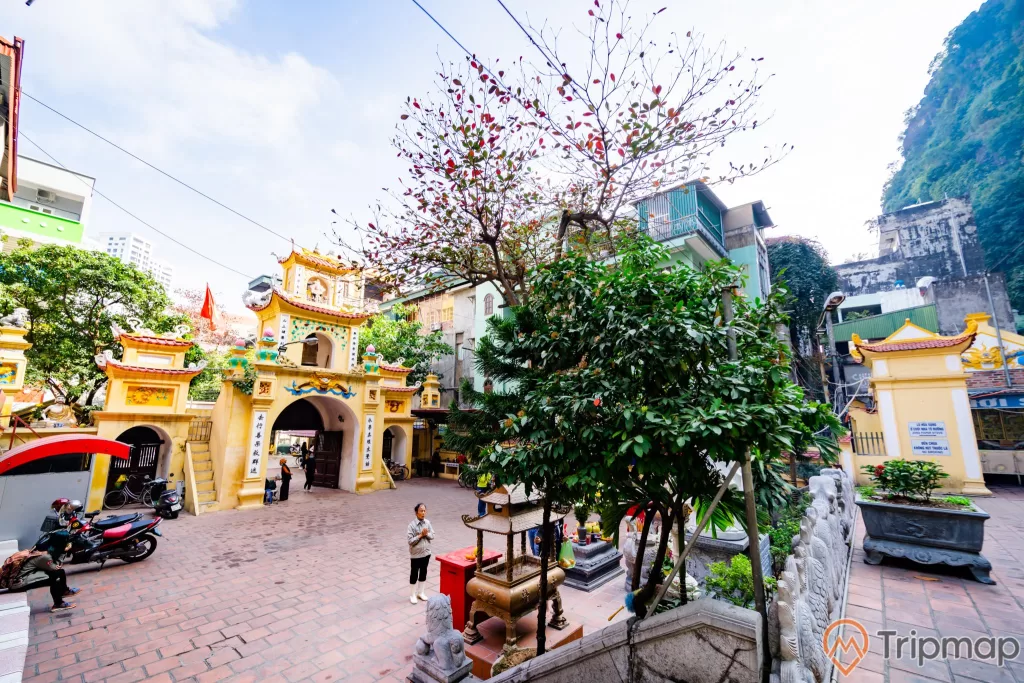 chùa Long Tiên, nền gạch màu đỏ, nhiều xe máy, nhiều cây xanh, cổng chùa sơn màu vàng, tượng kỳ lân bằng đá, ảnh chụp ban ngày