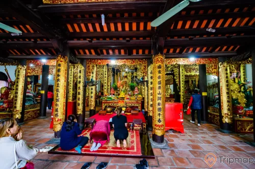 Chùa Long Tiên, nền gạch màu đỏ, nhiều người đang cầu nguyện, cây cột nhà có hoa văn màu vàng nhiều chữ hán, trần nhà bằng gỗ màu nâu, ảnh chụp ban ngày