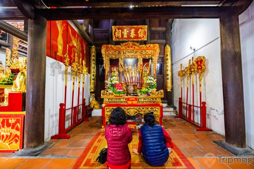 Chùa Long Tiên, Cung Trần Triều, nền gạch màu đỏ, người đang cầu nguyện, cây cột nhà màu nâu, hoa văn màu vàng có chữ hán