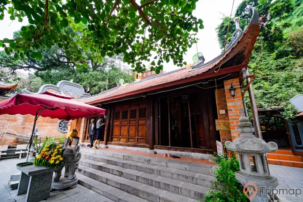 Đền thờ Đức Ông Trần Quốc Nghiễn, bậc thang màu xám, cánh cửa bằng gỗ màu nâu, nhiều cây xanh, ảnh chụp ban ngày