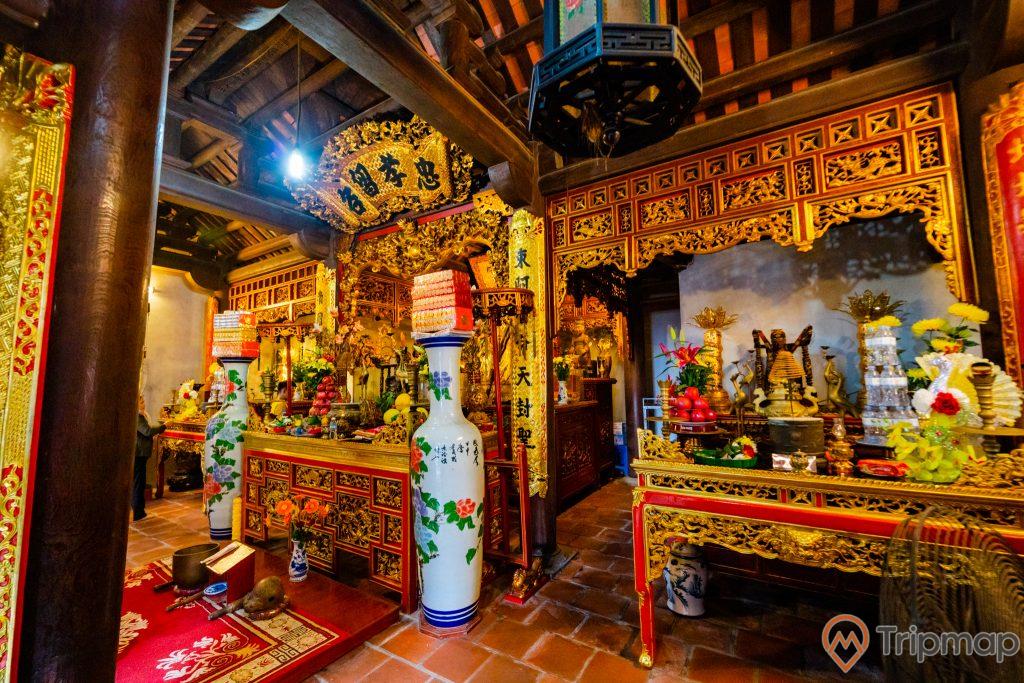 Đền thờ Đức Ông Trần Quốc Nghiễn, nền gạch màu đỏ, gian thờ có hoa văn màu vàng, nhiều chữ hán, cột nhà màu nâu, trần nhà bằng gỗ màu nâu