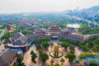Khu vui chơi giải trí Sun World Ha Long Complex, khuôn viên có nền gạch màu đỏ, nhiều cây xanh, tượng rồng màu vàng, nhà khách có mái ngói màu xám, khu trò chơi ở phía xa, đường ray màu trắng, ảnh chụp từ trên cao, ảnh chụp ban ngày