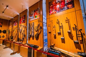 Bảo tàng Quảng Ninh, bộ dây bĩ kéo, bộ gẩy, các loại nhạc cụ được treo trên bức tường bằng gỗ màu nâu, nhiều bức tranh được treo trên tường bằng gỗ màu nâu, nền nhà bằng gạch màu trắng