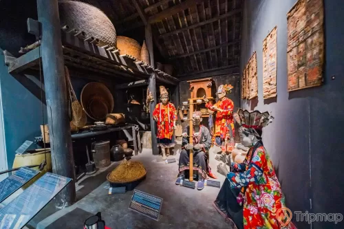 Khu tái hiện lịch sử hình thành mỏ than, bảo tàng Quảng Ninh, nhiều mô hình người đội mũ mặc áo đỏ, nền nhà màu nâu, nhiều dụng cụ nhà bếp bằng mây, tường nhà màu xám