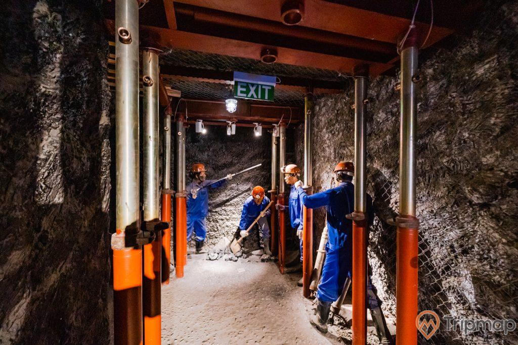 Khu tái hiện lịch sử hình thành mỏ than, bảo tàng Quảng Ninh, nhiều mô hình công nhân mặc quần áo xanh đang làm việc, nền đất màu xám, nhiều cây cột sắt sơn màu đỏ