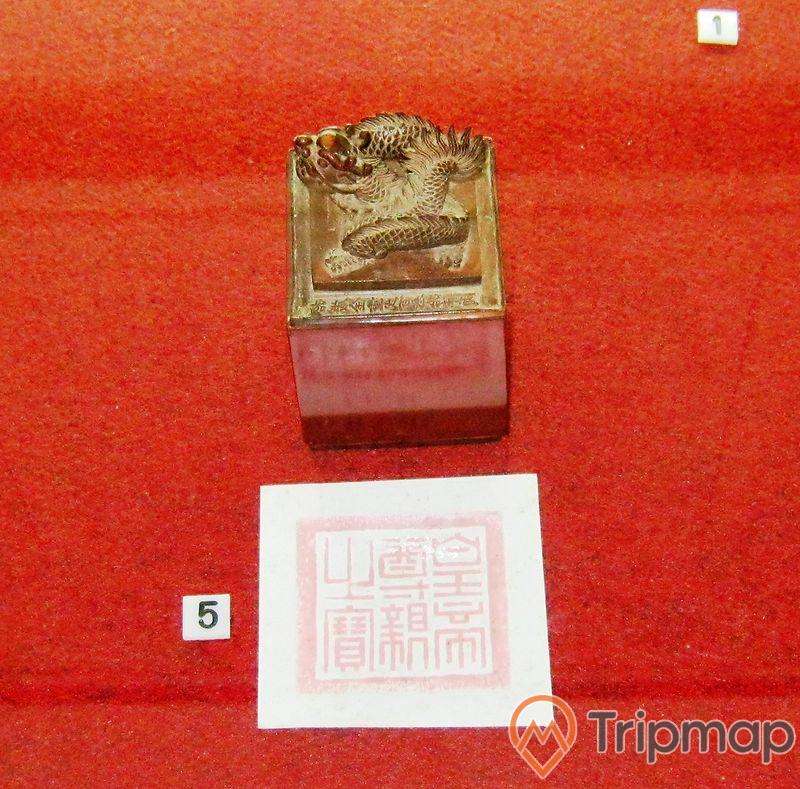 con dấu khắc hình con rồng và tờ giấy in dấu ấn đặt trên bàn màu đỏ