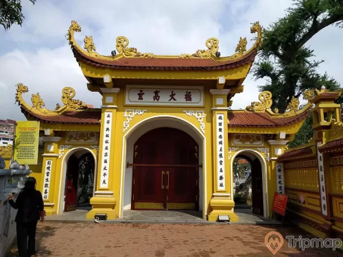 1 người đứng trước cổng tam quan phía ngoài của chùa Trấn Quốc, bầu trời có mây
