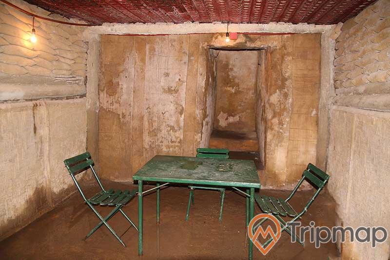 nơi bàn bạc trong hầm chỉ huy tướng Đờ Cát, bộ bàn ghế màu xanh lá cây, 2 chiếc bóng đèn tròn trên mái, ảnh chụp trong hầm