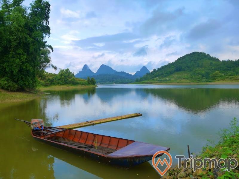 view Hồ Cấm Sơn, con thuyền ở cạnh bờ hồ, cây cối xanh tươi trên núi đồi ở phía xa, bầu trời nhiều mây