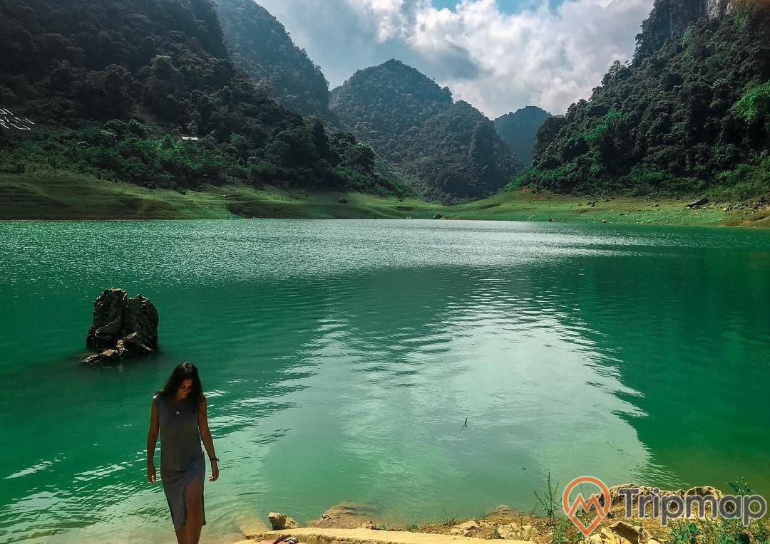 du khách đứng bên Hồ Thang Hen, cô gái mặc váy màu ghi đứng tạo dáng bên bờ hồ, bầu trời nhiều mây, ảnh chụp ngoài trời