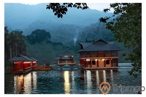 Nhà trên hồ khu du lịch Ao Vua, ngôi nhà bật đèn lun linh trên mặt hồ, cây cối ven hồ và trên đồi núi phía xa, ảnh chụp xế chiều