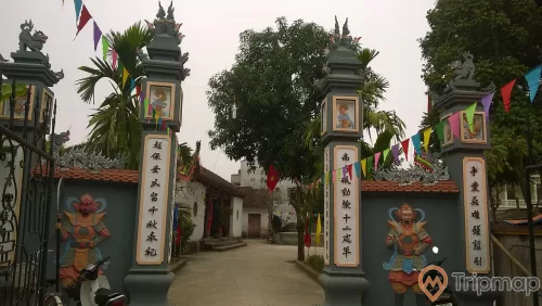 ảnh chụp trước cổng đền thờ Đinh Tiên Hoàng, 2 chiếc xe máy 1 chiếc xe đạp, 2 dây nhiều lá cờ màu sắc, cây trong sân đền