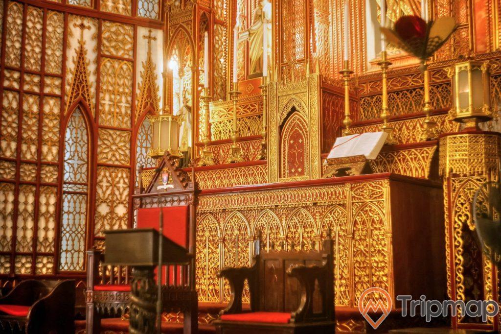 bàn thờ trong nhà thờ lớn hà nội sơn son thiếp vàng, có 1 quyến sách trên bàn thờ, 3 chiếc ghế gỗ, bàn thờ màu vàng và màu đỏ