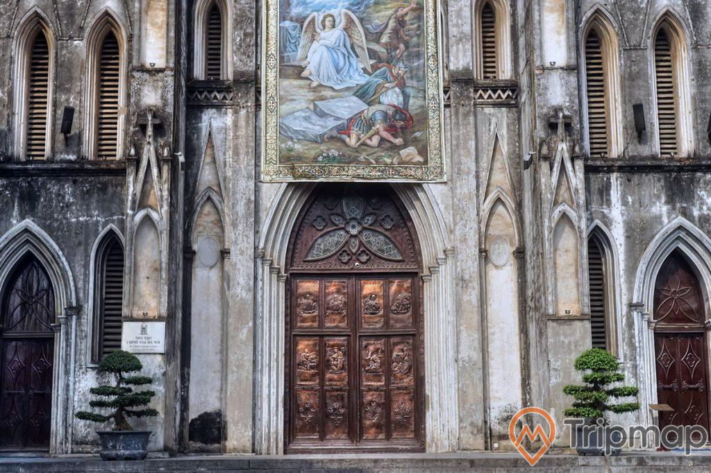 2 chậu cây cảnh bên cạnh cửa ra vào của nhà thờ lớn Hà Nội, một bức tranh lớn ở trên cánh cửa của nhà thờ lớn Hà Nội