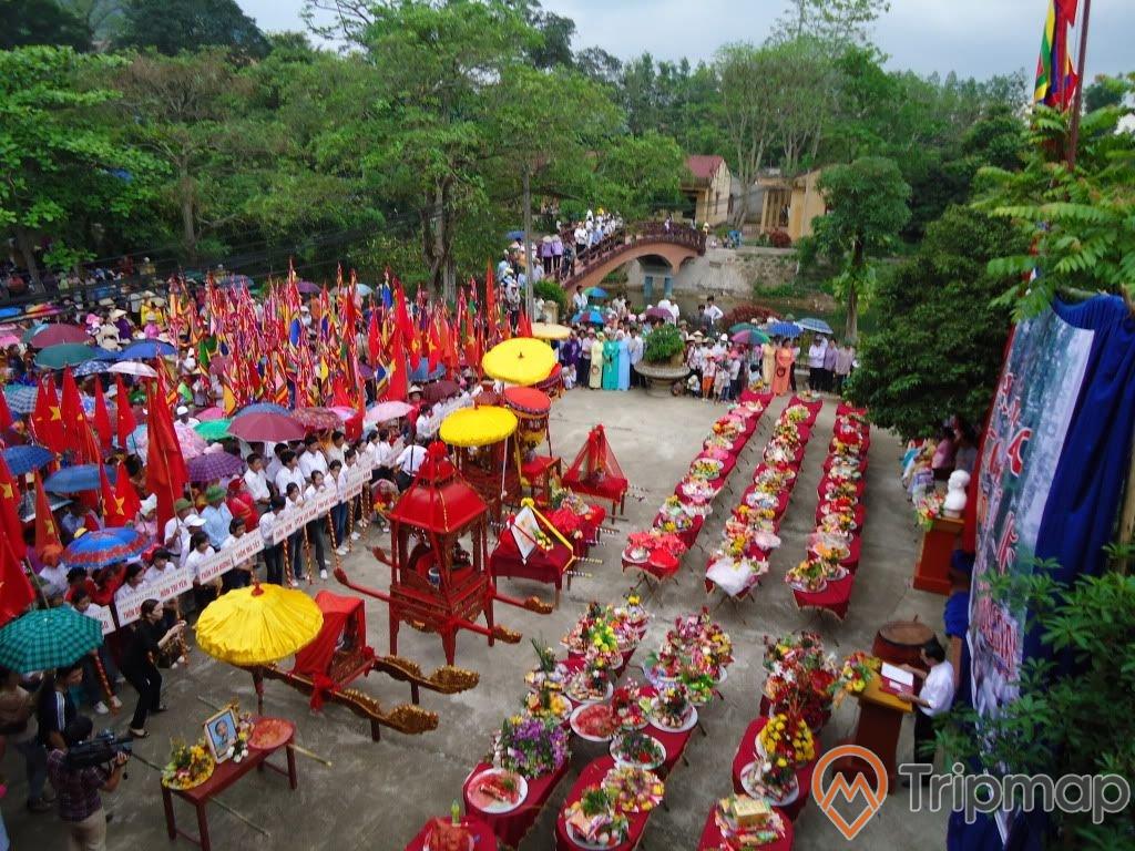 lễ hội đền suối mơ, mâm đồ thờ cúng đặt bàn trải thảm màu đỏ và kiệu màu đỏ có chiếc ô màu vàng ở trên sân đền, mọi người đang đứng giữa sân đền, phía xa có cây cầu và cây cối xanh tươi gần đền