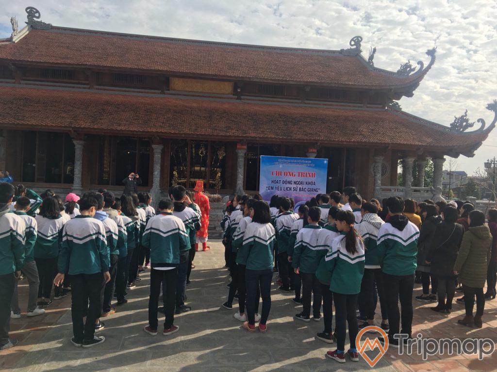 đoàn học sinh đi tham quan thành cổ Xương Giang, ngôi nhà 2 tầng mái ngói màu đỏ, nhiều học sinh đang đứng trên sân trước ngôi nhà, bầu trời nhiều mây và có nắng