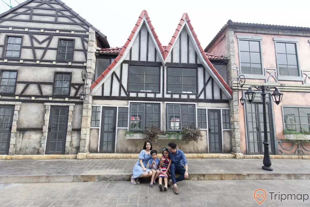 ngôi làng hoa Beuvron trong Thiên Đường Bảo Sơn, gia đình đang ngồi trước nhà tạo dáng chụp ảnh, 1 cây đèn trên vỉa hè, ảnh chụp ngoài trời