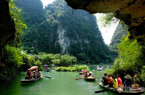 Quang cảnh trước hang động Phúc Long, mọi người ngồi trên thuyền đi trên dòng sông nước, núi đồi cây cối xanh tươi, ảnh chụp trong hang gần cửa động