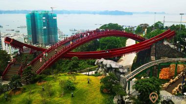 Cầu Koi, cầu sơn màu đỏ, nhiều người đang đi trên cầu, thảm cỏ màu xanh, nhiều cây xanh, tòa nhà đang được xây dựng ở phía xa, ảnh chụp ban ngày