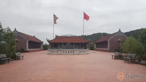 Miếu thờ Trần Khánh Dư, nền gạch màu đỏ, nhiều ghế đá màu xám, trời nhiều mây, lá cờ việt nam, miếu bằng gạch màu đỏ, nhiều cây xanh, ảnh chụp ban ngày