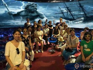 Rạp chiếu phim 12D, nhiều người đang trải nghiệm rạp phim, nền đường bằng tấm vải màu đỏ, bức tranh ngoài biển đằng sau