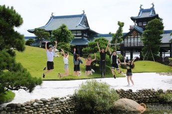 Vườn Nhật Bản Zen Garden, nhiều bạn trẻ đang nhảy trên nền đường màu xám, nhiều hòn đá to, nhiều cây xanh, nhà có mái ngói màu xanh, trời nắng, ảnh chụp ban ngày