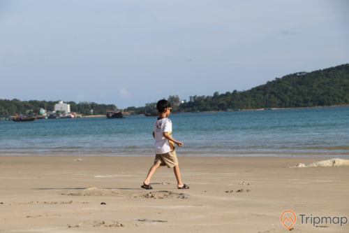 صبي يمشي على شاطئ الحب ، السماء الملبدة بالغيوم ، الصورة في الهواء الطلق ، الجزيرة في المسافة ، القارب في البحر في المسافة