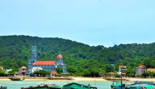 Đảo Thanh Lân, nhà thờ giáo họ, ngọn núi nhiều cây xanh phía xa, nhiều thuyền đang đỗ trên bãi biển, trời nắng, ảnh chụp ban ngày