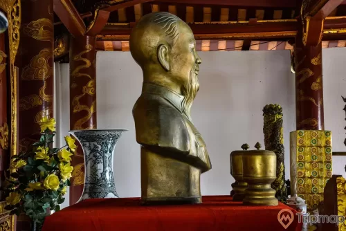 Mặt bên phải bức tượng Bác Hồ trong đền thờ Bác Hồ tại khu di tích lưu niệm Hồ Chủ tịch trên đảo Cô Tô, tượng đồng bác Hồ và 3 lư bằng đồng trên bàn màu đỏ, chiếc lục bình và bình hoa màu vàng cạnh bàn thờ, ảnh chụp trong đền thờ Bác Hồ