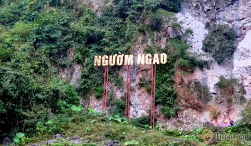 bảng tên Động Ngườm Ngao cạnh chân núi, cây cối xanh tươi, ảnh chụp ngoài trời