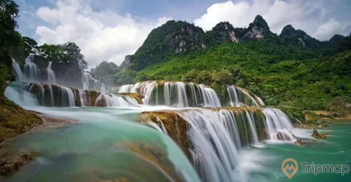 thác bản giốc đang chảy, cây cối xanh tươi, bầu trời nhiều mây trắng, ảnh chụp ngoài trời gần thác nước