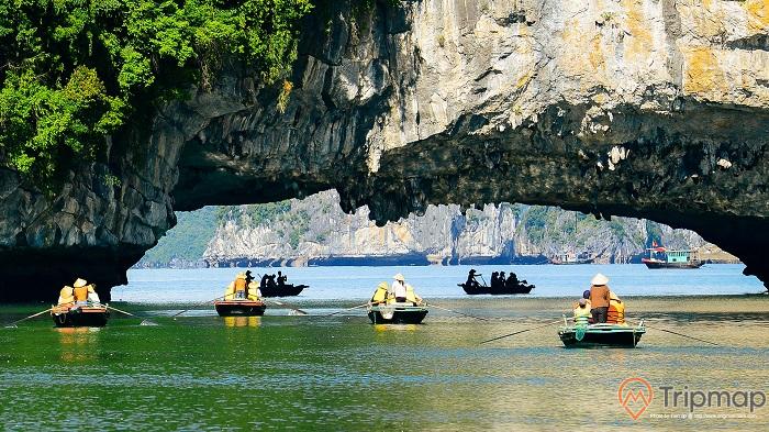 a group of people in boats in a body of water by a large rock cliff